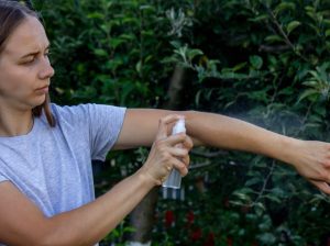 a woman applying repellent spray to her arm.