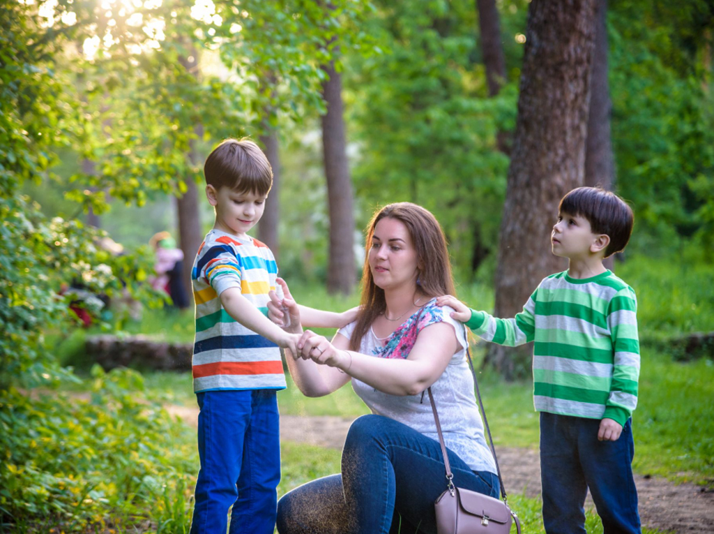 a mother applying insect repellent to her two sons.